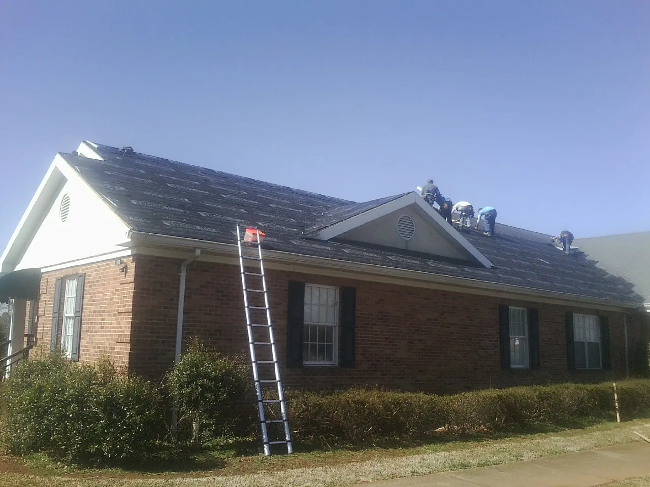Crew tearing shingles off a brick ranch roof with a ladder set — Metal Roof Repair work by our crew in Pittsfield