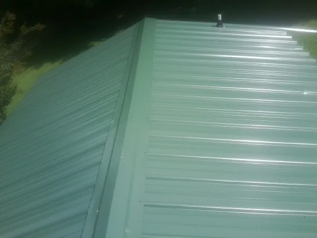 New green metal panels meeting at the ridge of a roof — Flat Roof Repair work by our crew in Pittsfield