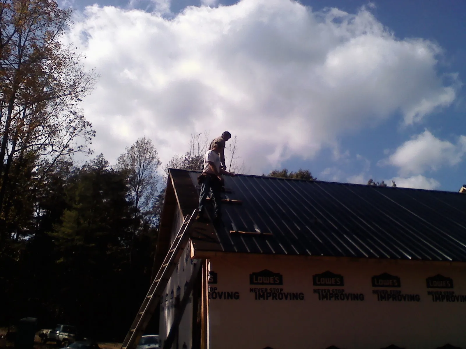 Roofer fastening dark metal panels high against a cloudy sky, from a Roof Inspection job in Pittsfield